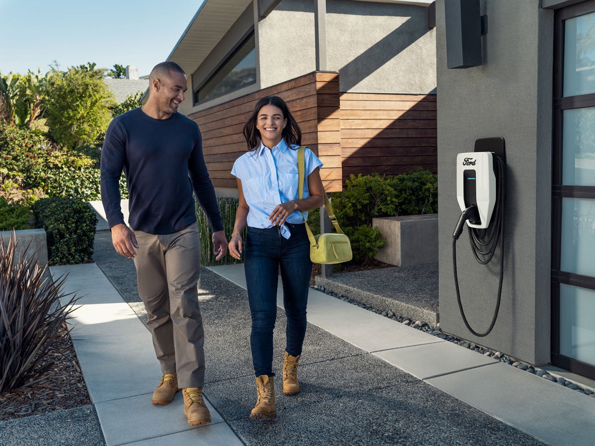 A couple walking out of their home with a Ford Charge Station Pro attached to their garage in the background